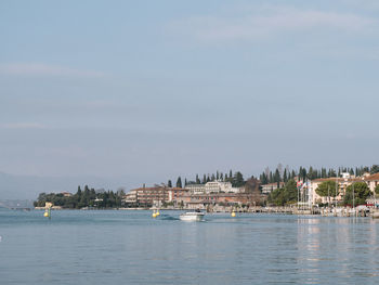 Sailboats in sea by buildings against sky