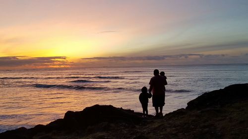 Silhouette family standing at beach during sunset