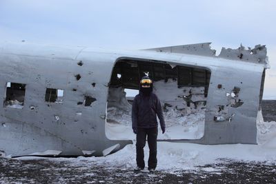 Full length portrait of person standing by damaged airplane at beach during winter