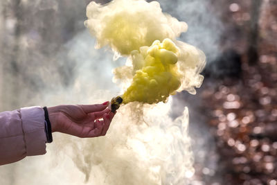 Cropped hand holding distress flare emitting smoke