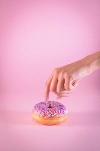 Hand holding ice cream cone against pink background