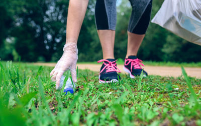 Low section of woman picking plastic bottle at park