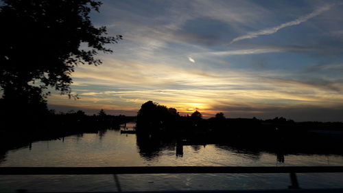 Silhouette trees by lake against sky during sunset