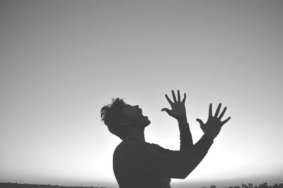 Side view of man screaming while gesturing against sky during sunset