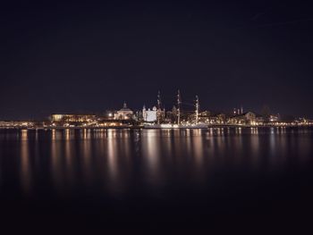 Illuminated buildings by sea against sky at night