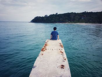 Rear view of man sitting on pier in sea