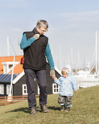 Grandfather and granddaughter walking on field against sky