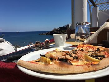 Close-up of pizza in plate on table by sea against clear blue sky