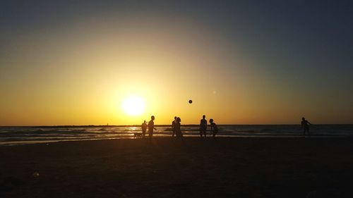 Silhouette friends playing with ball at beach against sky during sunset