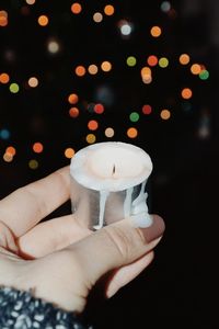 Cropped hand holding candle against defocused lights at night