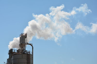 Low angle view of factory emitting smoke against clear blue sky