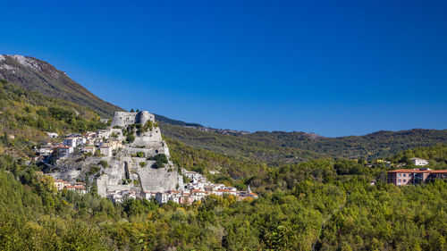 Panoramic view of townscape by mountain against clear blue sky