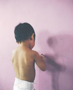 Rear view of shirtless boy standing against wall