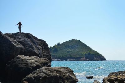 Man standing on cliff by sea against clear sky