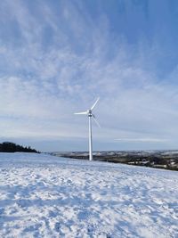 Wind turbines on snow covered field against sky
