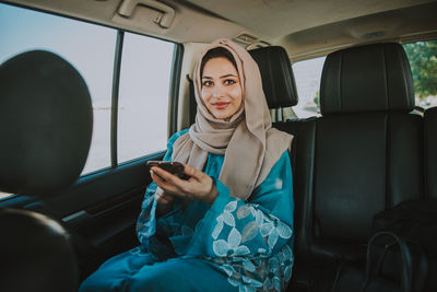 Young smiling woman using phone while sitting in car