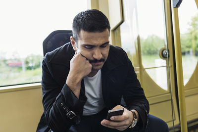Young man text messaging through mobile phone in tram