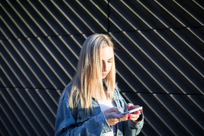 Beautiful young woman using phone standing against wall