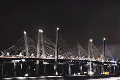 Illuminated bridge over river against sky at night