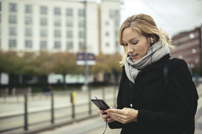 Mid adult businesswoman listening music through smart phone at tram station