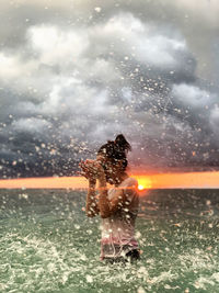 Blurred motion of woman splashing water against sky during sunset