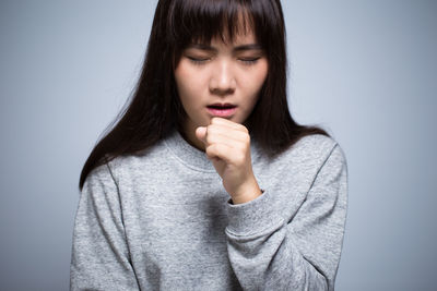 Beautiful young woman coughing against gray background