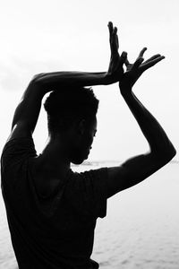 Silhouette young man dancing at beach against clear sky