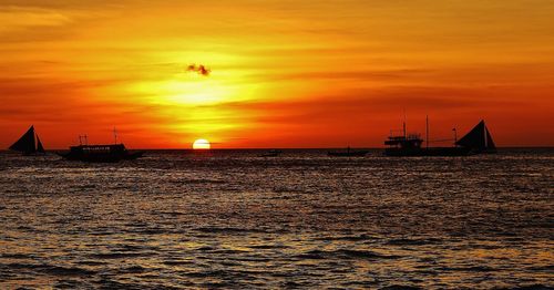 Silhouette boats sailing in sea against orange sky