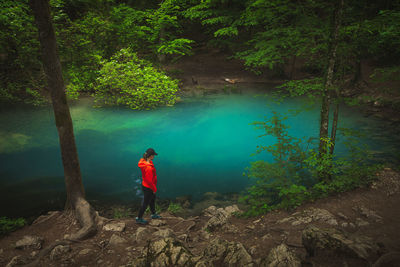 Woman dressed in a red jacket near a clear water lake in the heart of nature. 