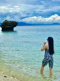 Rear view of woman standing in sea against sky