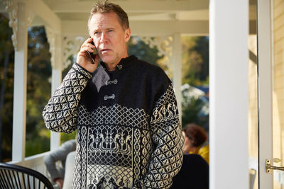 Mature man looking away while answering smart phone on porch