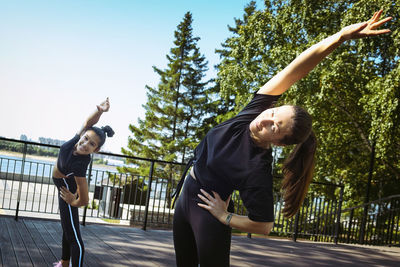 Girl in sportswear on a sunny summer day on the embankment in the park doing fitness and stretching