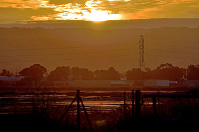 Silhouette electricity pylon against sky during sunset