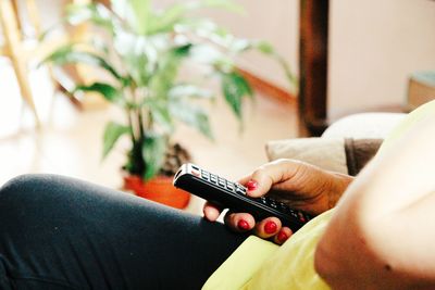 Midsection of woman holding remote control while sitting on sofa at home