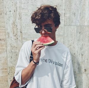 Young man eating food against wall