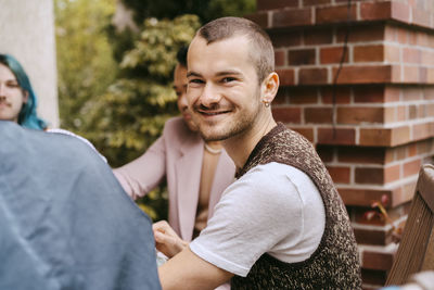 Side view portrait of smiling gay man sitting with friends during party in back yard