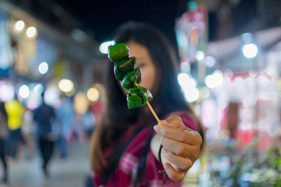 Close-up of woman holding food in skewer at night
