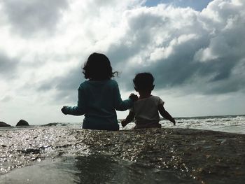 Rear view of siblings in sea against sky