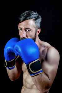 Portrait of boxer wearing boxing gloves standing against black background