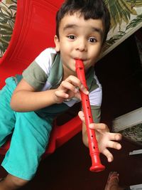 Portrait of cute boy playing flute while sitting on chair