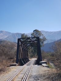 Railroad tracks leading towards mountains against clear sky