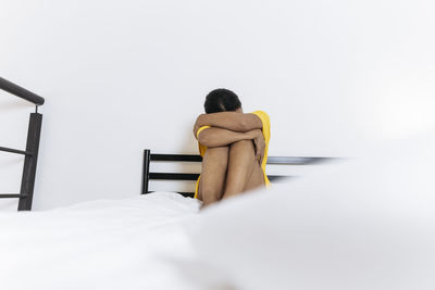 Sad young woman sitting on bed hugging knees