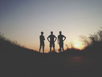 Silhouette male friends standing on field against sky during sunset