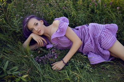 Teenage girl with dyed purple hair and a nose piercing in the grass,  flowers and in a short dress