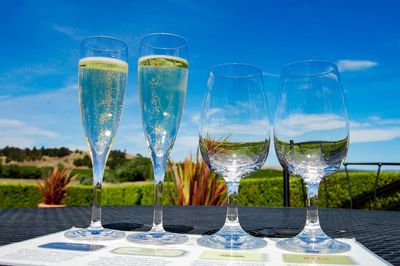 Low angle view of wineglass and champagne flutes on table against blue sky