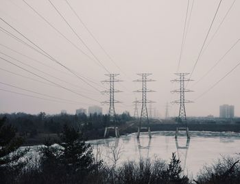 Electricity pylon by trees against sky