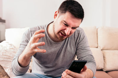 Young man using mobile phone while sitting on sofa at home
