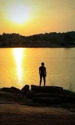 Silhouette man standing by lake against sky during sunset