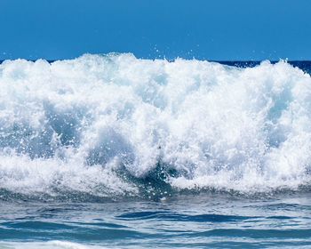 Waves splashing on shore against clear sky