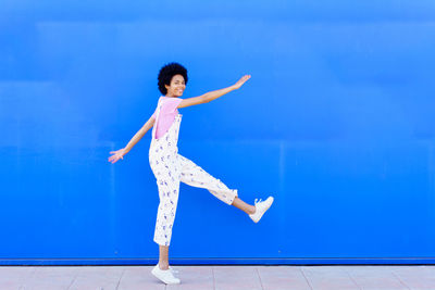 Full length of young woman jumping against blue sky
